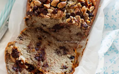 Fetta di banana bread con gocce di cioccolato e noci, guarnita con mandorle e nocciole tritate.