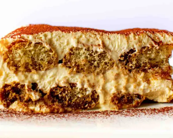 Una fetta di tiramisù, con strati di savoiardi inzuppati e crema al mascarpone, spolverata di cacao. La ricetta perfetta per un dolce indimenticabile.