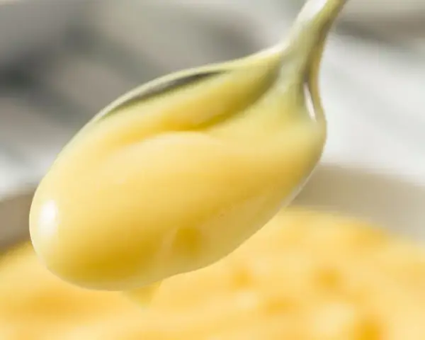 Crema pasticcera lucida su un cucchiaio. Il burro la rende vellutata e lucida, perfetta per farcire dolci.
