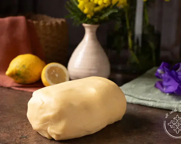 Impasto di pasta frolla che non si rompe, pronto per creare dolci perfetti. Accanto, limoni freschi e un tocco di colore.