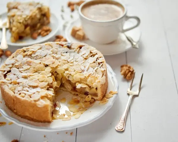 Torta con mandorle e zucchero a velo, perfetta per una ricetta frangipane. Accanto, una tazza di caffè e una fetta di torta.