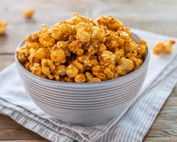 Una ciotola piena di pop corn caramellati, dorati e invitanti, su un tovagliolo a righe.