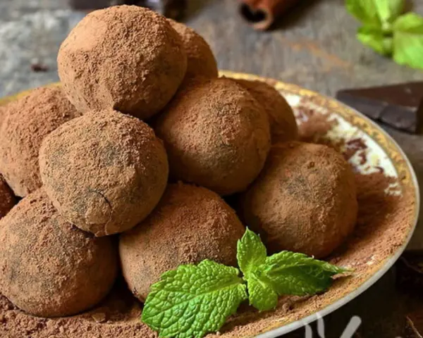 Pile di tartufi al cioccolato facili e veloci, spolverati di cacao, con menta fresca e un pezzetto di cioccolato fondente.