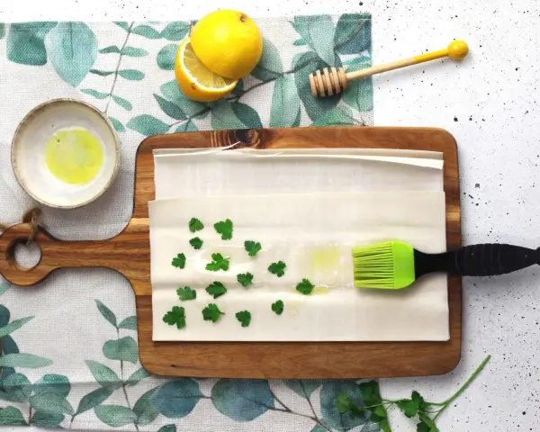Preparazione per un piatto con pasta fillo: ingredienti come limone, miele, prezzemolo e olio su un tagliere.