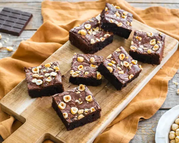 Deliziosi brownie senza glutine con nocciole tostate su tagliere di legno.