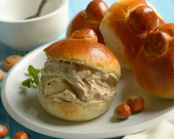 Brioches col tuppo, soffici e dorate, ripiene di gelato cremoso. Un dolce siciliano da gustare con nocciole e menta.