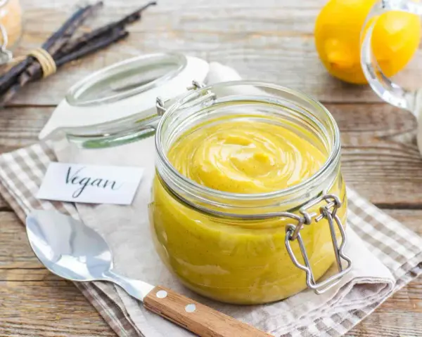 Crema pasticcera vegana in un barattolo di vetro, con bacche di vaniglia e limoni sullo sfondo.