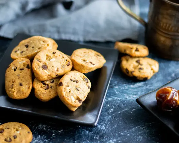 Biscotti vegan con gocce di cioccolato e datteri su piatti neri, pronti per una pausa golosa.