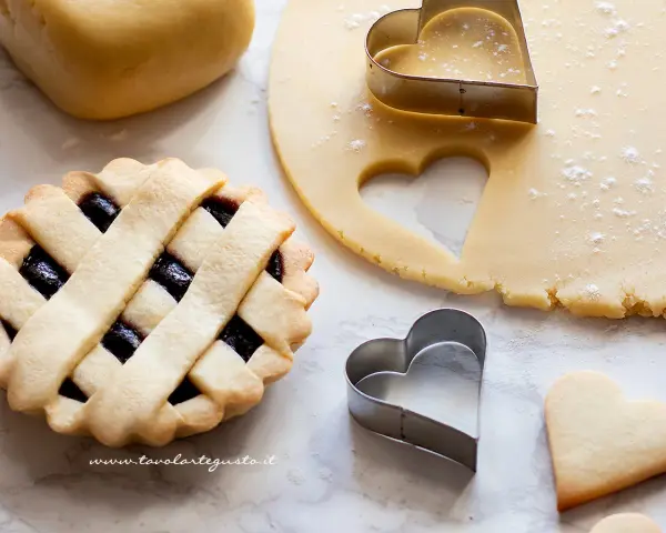 Una crostata con ripieno di marmellata, pasta frolla stesa e tagliabiscotti a forma di cuore.