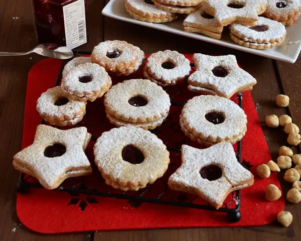 Deliziosi biscotti Linzer, a forma di stella e tondi, ripieni di marmellata e spolverati di zucchero a velo, su una griglia nera.