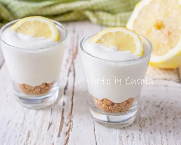 Due bicchierini di mousse al limone con base croccante e fetta di limone, su un tavolo di legno.