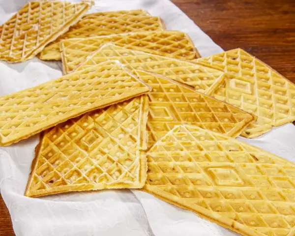 Un mucchio di croccanti ferratelle abruzzesi, dolci tradizionali, disposte su un panno bianco su un tavolo di legno.