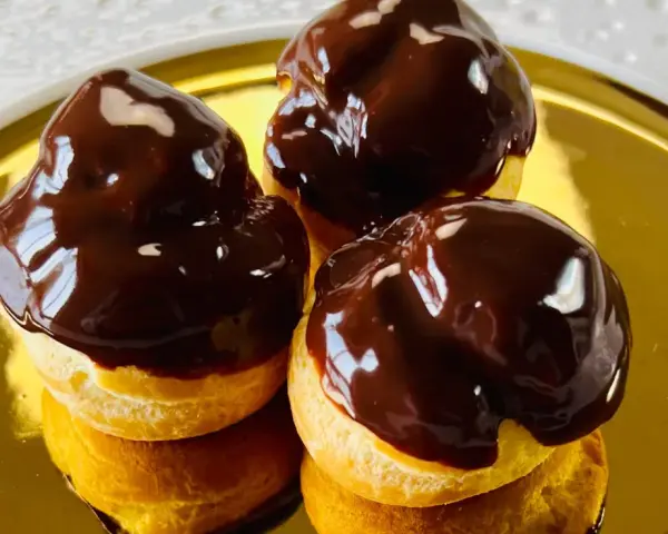 Tre golosi bignè al cioccolato, lucidi e invitanti, su un piatto dorato.