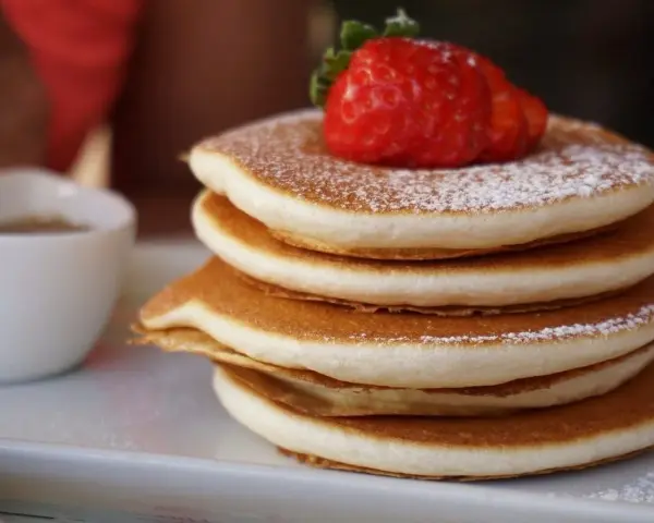 Pancake Bimby perfetti, impilati e spolverati di zucchero a velo, con una fragola fresca in cima.