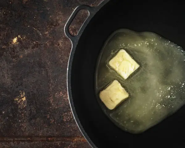 Due cubetti di burro a pomata si sciolgono in una padella, pronti per creare una base saporita.
