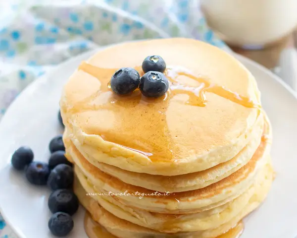 Pancakes soffici con albumi, guarniti con mirtilli freschi e sciroppo d'acero. Un dolce inizio di giornata.