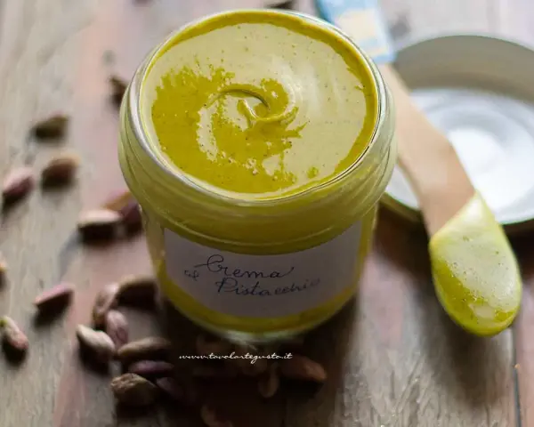 Vasetto di crema di pistacchio fatta in casa, con pistacchi sparsi intorno. La ricetta perfetta per una delizia!