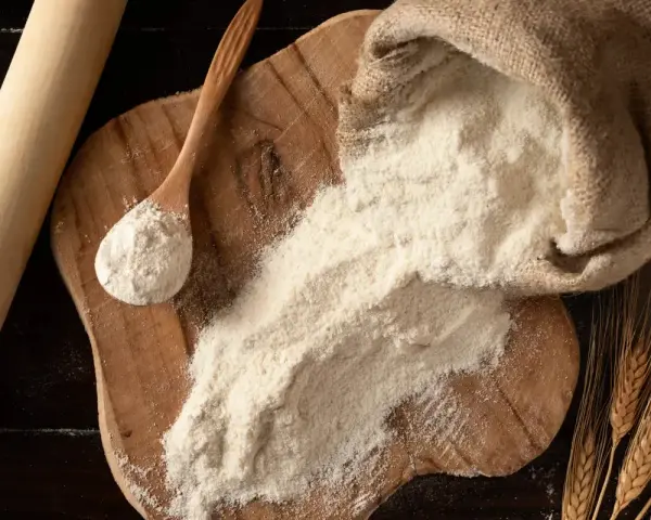 Farina 0 al posto della 00 nei dolci: un sacco di farina, un mestolo e spighe di grano su un tagliere di legno.