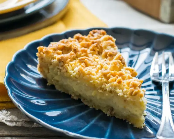 Fetta di sbrisolona con crema pasticcera su piatto blu, con forchetta trasparente.