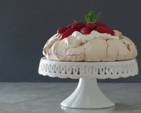 Pavlova ricetta: meringa croccante fuori e morbida dentro, guarnita con panna montata e fragole fresche.