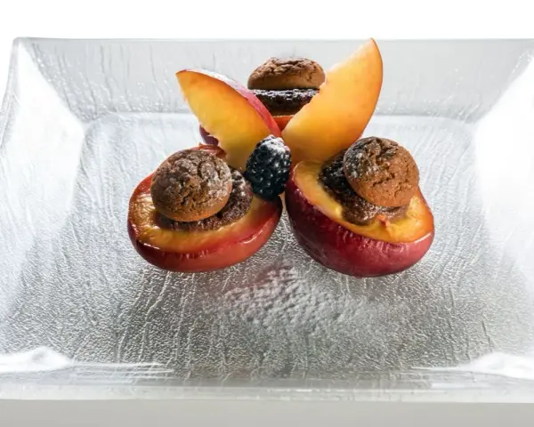 Deliziose pesche ripiene con biscotti e frutti di bosco, un dolce invitante su un piatto di vetro.