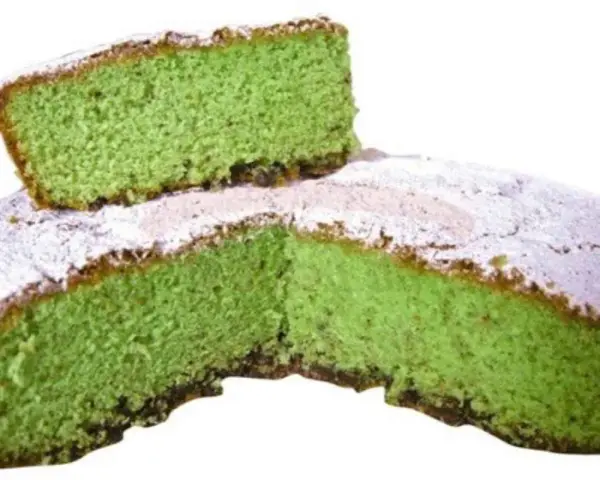 Una fetta di torta alla menta verde brillante, cosparsa di zucchero a velo, è appoggiata su una torta intera.