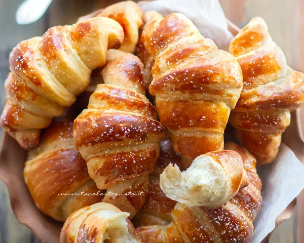 Brioches fatte in casa, dorate e soffici, cosparse di zucchero a velo. Un profumo invitante che ricorda la colazione perfetta.