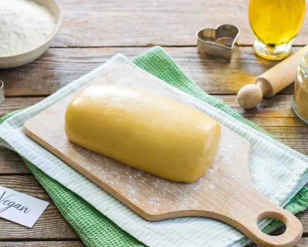 Impasto giallo pronto per biscotti, con un'etichetta "Vegan" e ingredienti come farina, zucchero e olio.