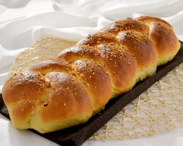 Treccia dorata di dolci con farina manitoba, cosparsa di granella croccante, su un letto di lino bianco.