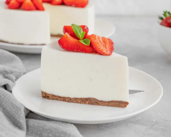 Una fetta di torta fredda allo yogurt senza biscotti, guarnita con fragole fresche e menta, su un piatto bianco.