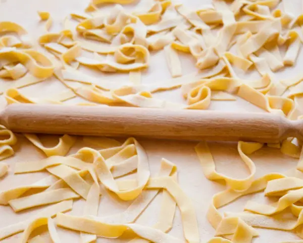 Fettuccine fresche sparse su un piano di lavoro, con un mattarello in legno. La farina, che è all-purpose flour, è visibile sulla pasta.