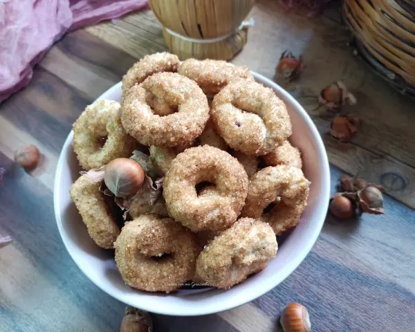 Ciambelline al vino cosparse di zucchero, con nocciole sparse sul tavolo di legno.