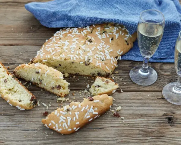 Fette di ciambella romagnola, cosparse di zuccherini, accanto a due bicchieri di spumante.