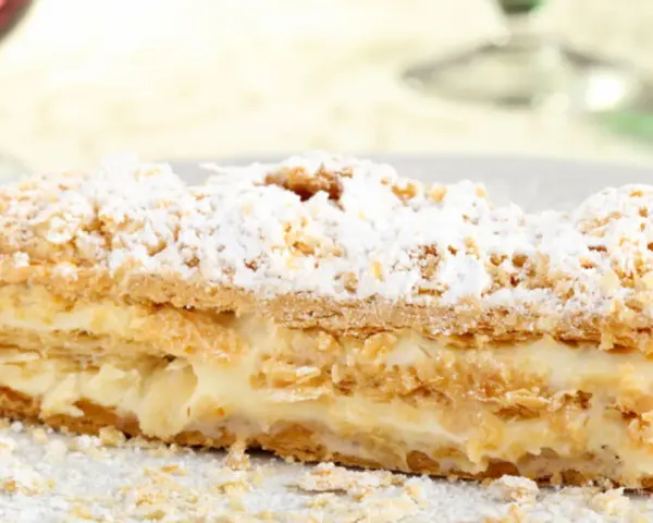 Una fetta di rettangolare torta millefoglie compleanno, con crema pasticcera e zucchero a velo.