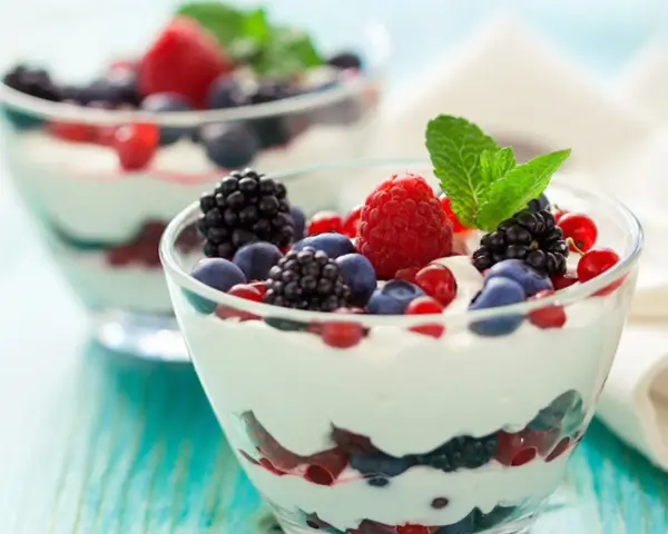 Deliziosa mousse allo yogurt con frutti di bosco freschi e una fogliolina di menta, servita in coppette di vetro.