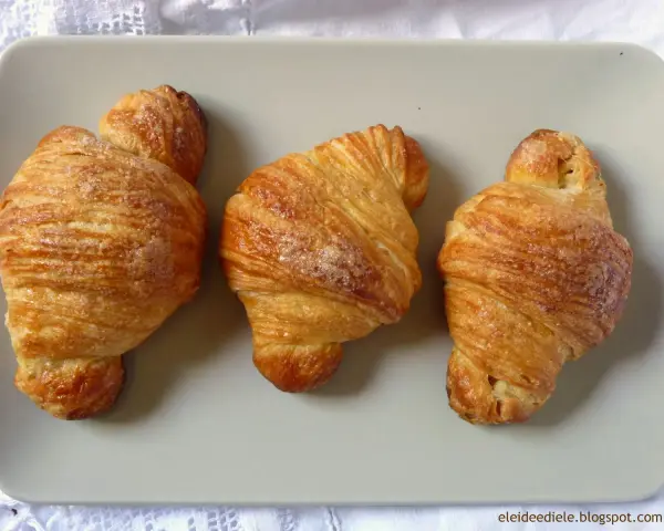 Tre deliziosi croissant dorati, cosparsi di zucchero, disposti su un piatto grigio.