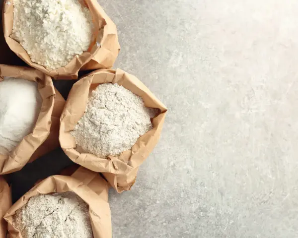 Sacchetti di carta aperti pieni di diverse farine, tra cui farina 0 e manitoba, pronte per creare pane e dolci.