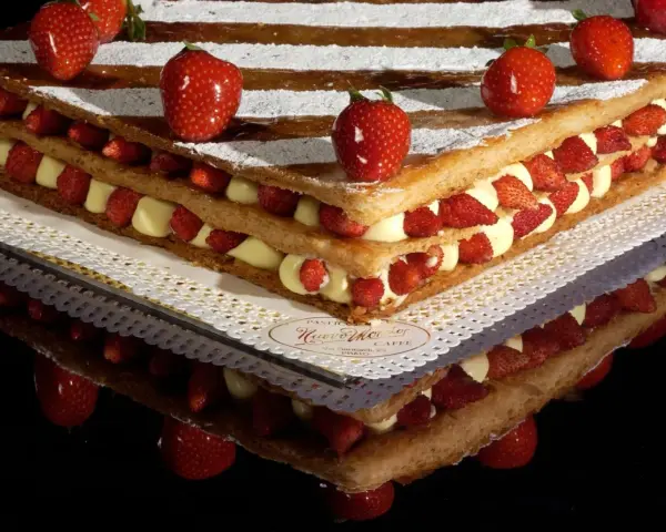 Un invitante millefoglie cake con strati di crema pasticcera e fragole fresche, decorato con fragole intere e zucchero a velo.