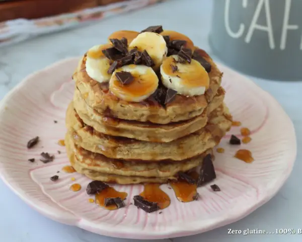 Pancake light con banana, cioccolato e sciroppo d'acero su un piatto rosa.