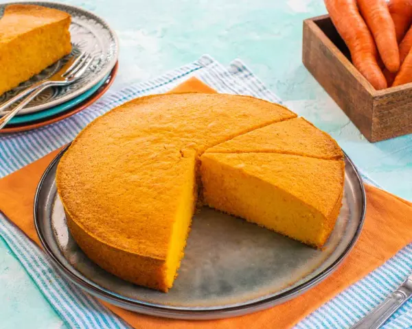 Una deliziosa torta di carote, appena sfornata, è tagliata a fette su un piatto. Accanto, un cesto di carote fresche.