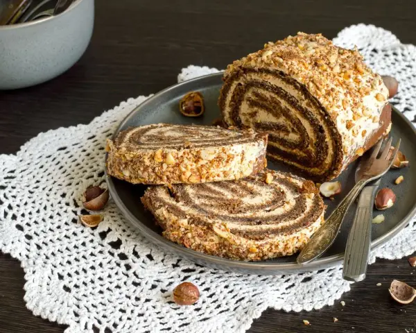 Rotolo alla Nutella ricoperto di granella di nocciole, servito su un piatto con due fette tagliate.