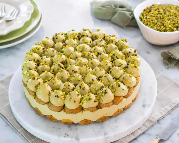 Torta rotonda con tante piccole meringhe verdi, guarnite con granella di pistacchio. Un delizioso tiramisù al pistacchio pronto per essere gustato.