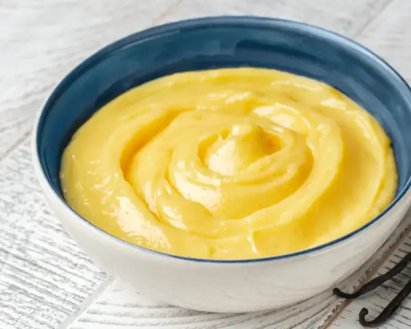 Una ciotola di crema gialla, liscia e invitante, con baccelli di vaniglia accanto. Perfetta per ogni ricetta crema.