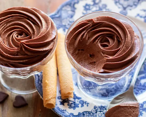 Deliziosa mousse al cioccolato in coppette di vetro, accompagnata da biscotti arrotolati e cuoricini di cioccolato.