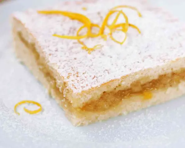 Fetta di crostata di frutta con pasta frolla, guarnita con zucchero a velo e scorza d'arancia. Perfetta per uno stampo da 28 cm.