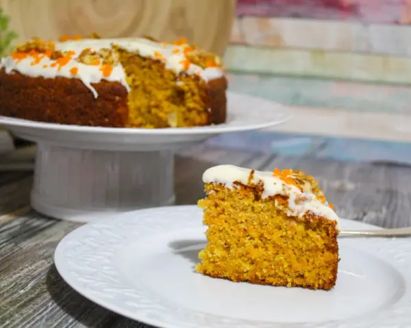 Una fetta di torta di carote senza glutine, soffice e profumata, con glassa bianca e decorazioni arancioni.