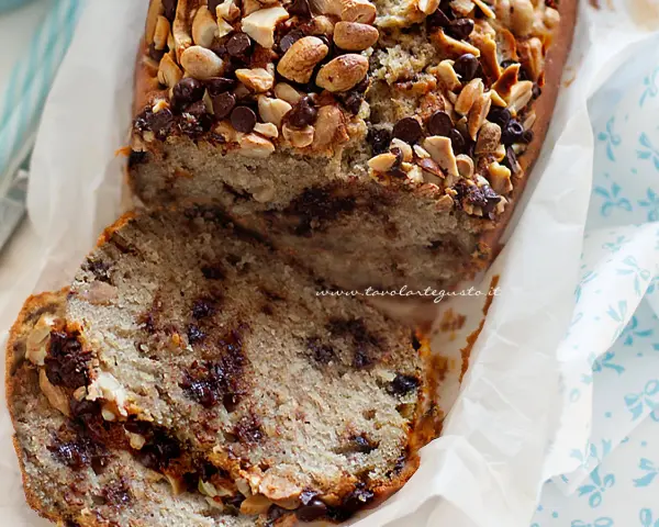 Fetta di banana bread con gocce di cioccolato e noci, guarnita con mandorle e nocciole tritate.