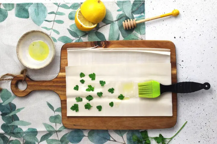 Preparazione per un piatto con pasta fillo: ingredienti come limone, miele, prezzemolo e olio su un tagliere.