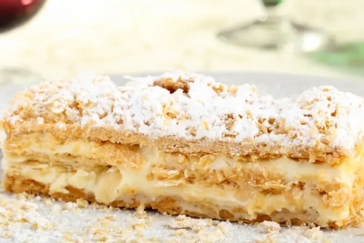 Una fetta di rettangolare torta millefoglie compleanno, con crema pasticcera e zucchero a velo.