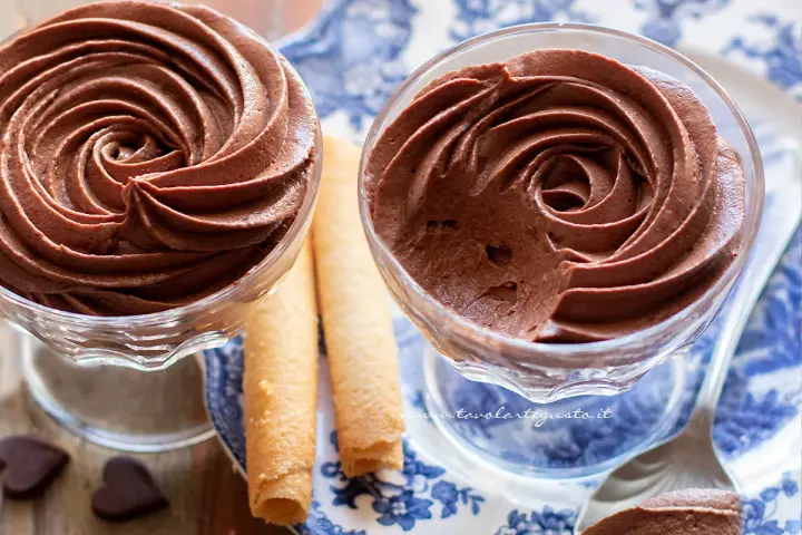 Deliziosa mousse al cioccolato in coppette di vetro, accompagnata da biscotti arrotolati e cuoricini di cioccolato.